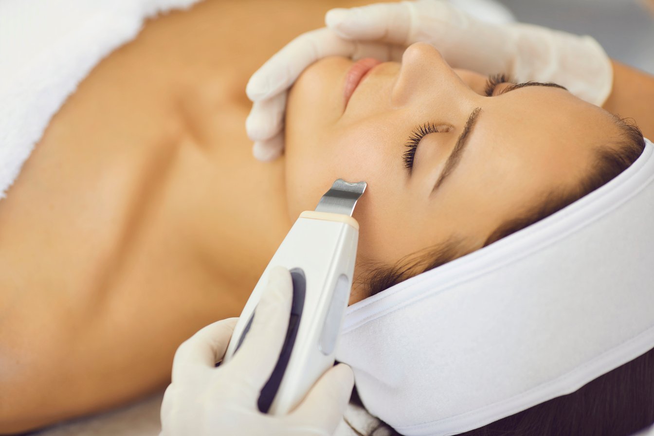Hands of Cosmetologist Making Ultrasound Facial Cleaning with Special Machine for Relaxing Woman